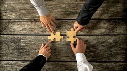 Four successful business men joining two puzzle pieces each bein