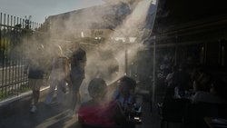 Des personnes passent devant un brumisateur pour se rafraîchir pendant une chaude journée dans le quartier de Monastiraki à Athènes.
