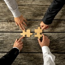Four successful business men joining two puzzle pieces each bein