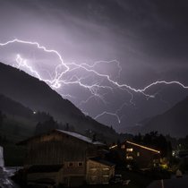 Un éclair ramifié fend le ciel orageux au-dessus de la vallée en direction de Gsteig; photo prise mi-juillet 2026 près de Gstaad (BE).