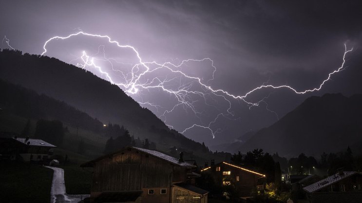 Un fulmine ramificato squarcia il cielo tempestoso sopra la valle in direzione di Gsteig; foto scattata a metà luglio 2026 nei pressi di Gstaad (BE).