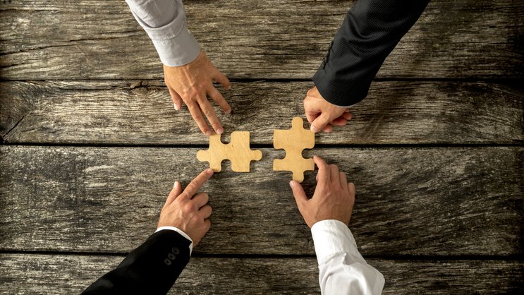 Four successful business men joining two puzzle pieces each bein